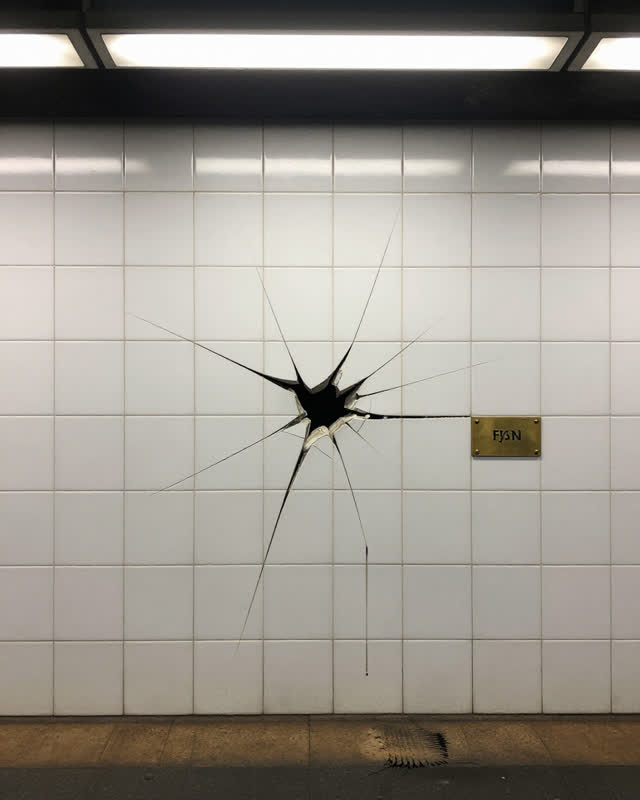 I dream of an underground subway station platform wall where one white ceramic tile carries a radiating impact crack fro
