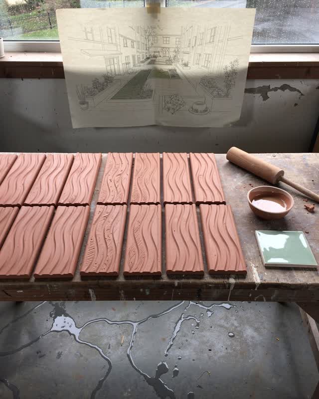 I dream of a community ceramic workshop where wet clay channel tiles for a public courtyard lie on a worktable, their gr