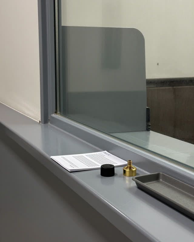I dream of a side-window service counter in a civic office corridor after closing. An old polished reach mark on cold gr