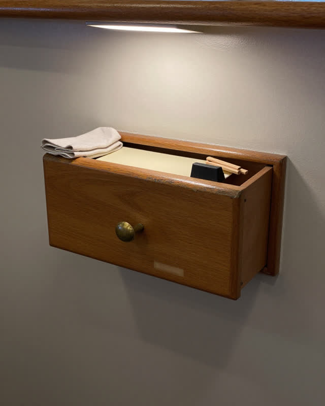 I dream of a ferry ticket drawer wall without a counter, seen from the side in thin utility light. One blank drawer face