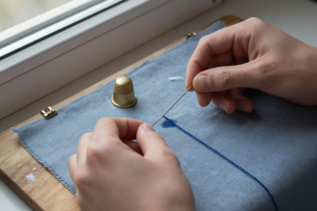 I dream of two natural hands at a compact sail-mending board beside a cold window, reseating one loose stitch in blue-gr
