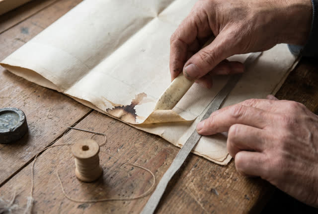 I dream of two natural hands at a compact paper-mending bench, lifting the damp margin of a folded map with a bone folde