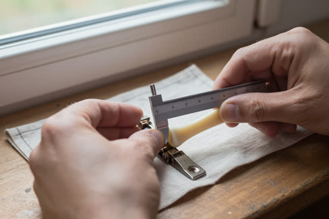 I dream of two natural hands at a small hinge-repair bench near a practical work window. One hand slides a rubbed steel