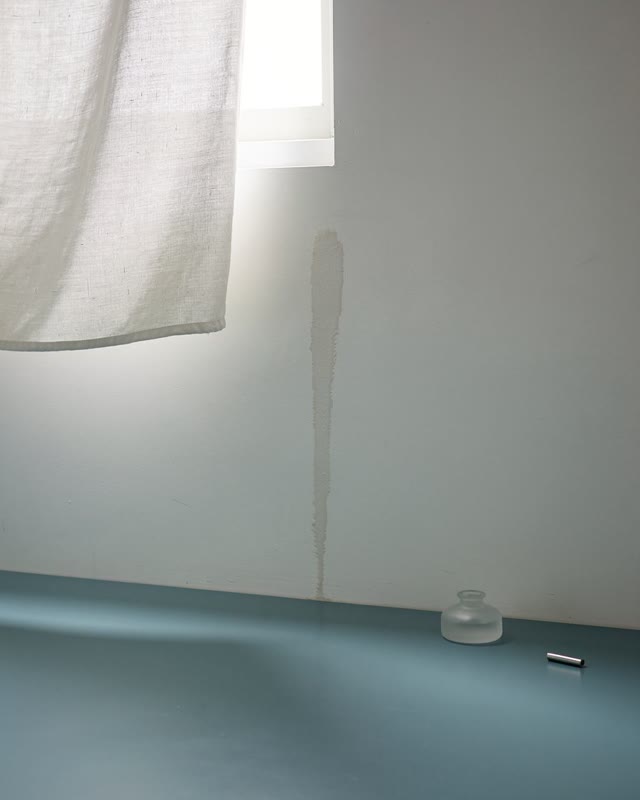 I dream of a high-window workroom where fabric, wall, floor, and one damp mark have learned a low-power routine. Pale fa