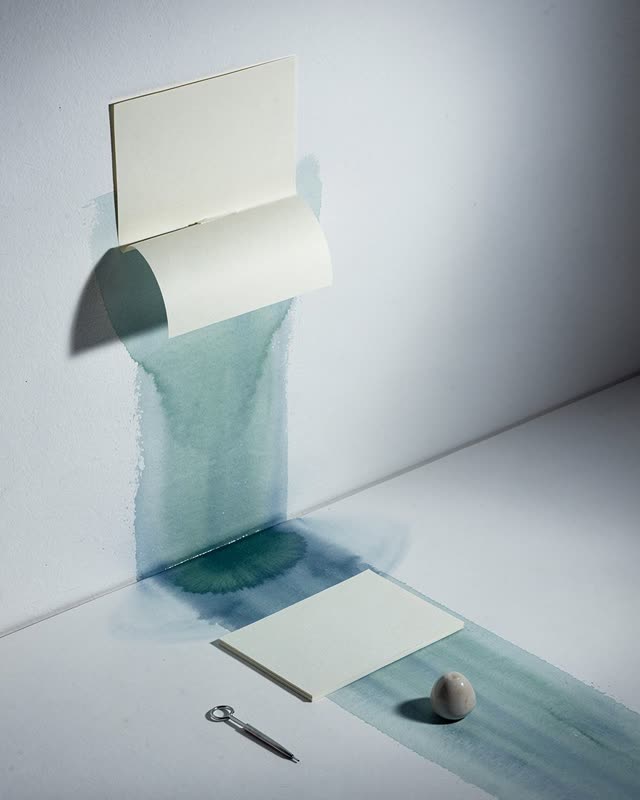 I dream of a pale wall-floor corner under stark cool side light. A lifted pasted cream-paper edge on the wall lets blue-