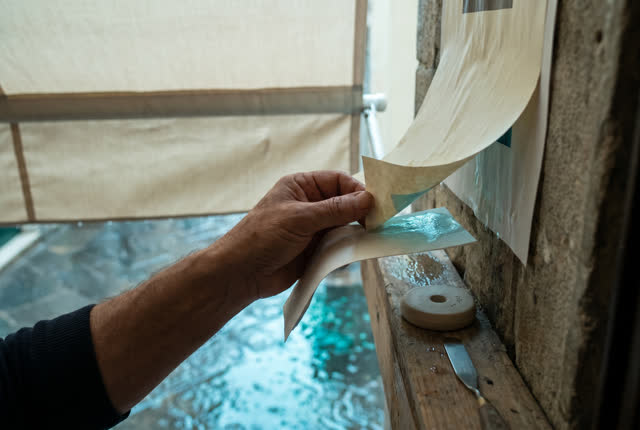 I dream of one natural hand at a sheltered exterior landing, shielding a lifted pasted corner before reflected rain ligh