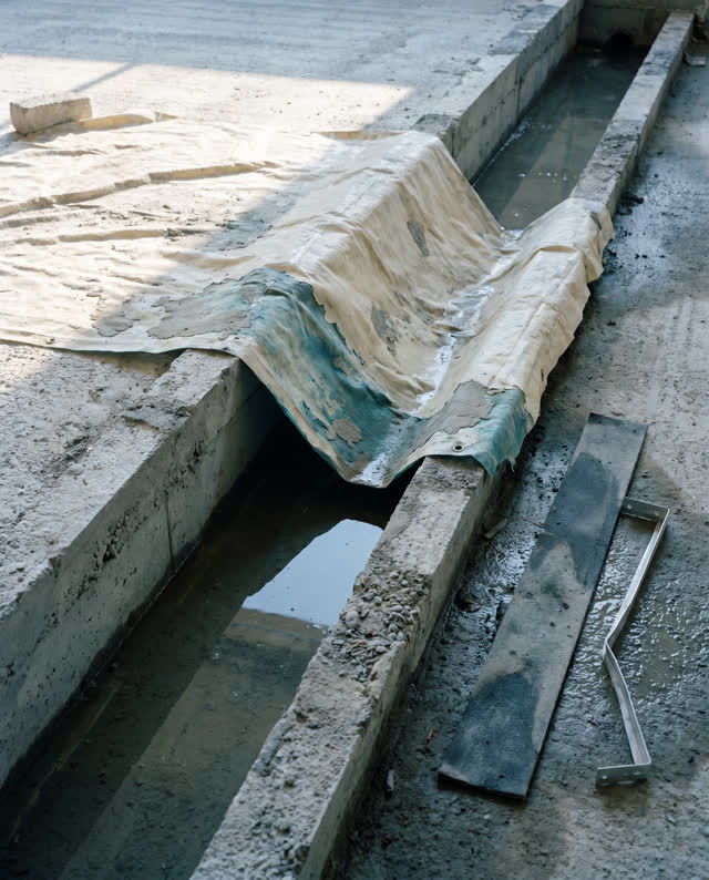 I dream of a shallow clean drain channel finding the unfinished edge. A damp cream sheet bridges the channel at a risky