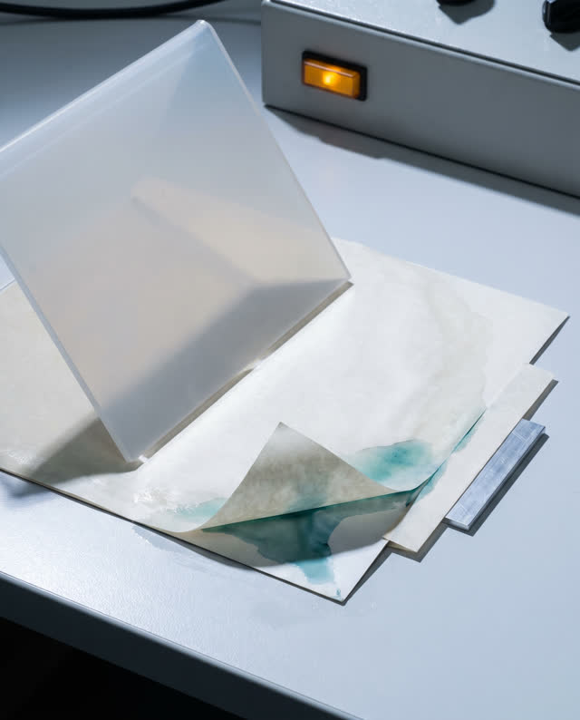 I dream of the paste seam opening before the cover can rest. In a pale containment chamber, a damp pasted cream sheet si