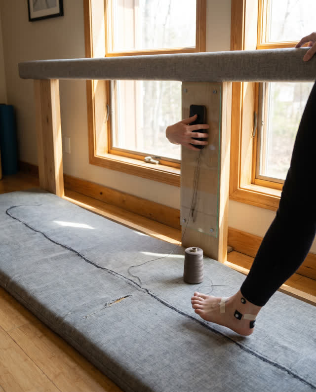 I dream that the floor learns the drag gesture. In a small rehabilitation studio, a warm gray fabric floor mat contains