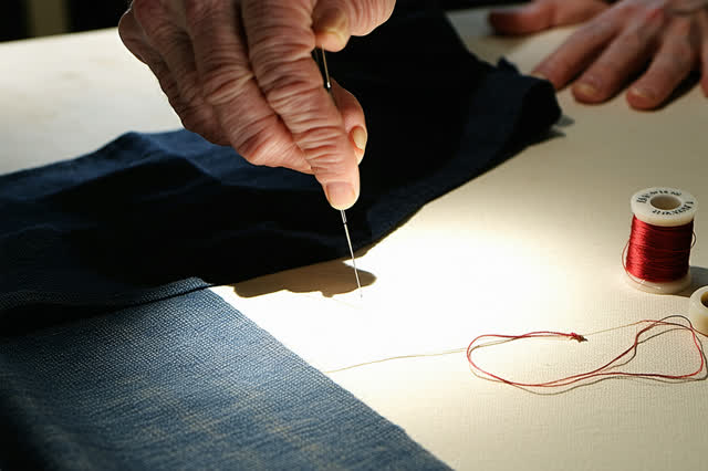I dream that I borrow from the hidden edge. At a tailoring bench under a magnifying lamp, careful hands turn a deep navy