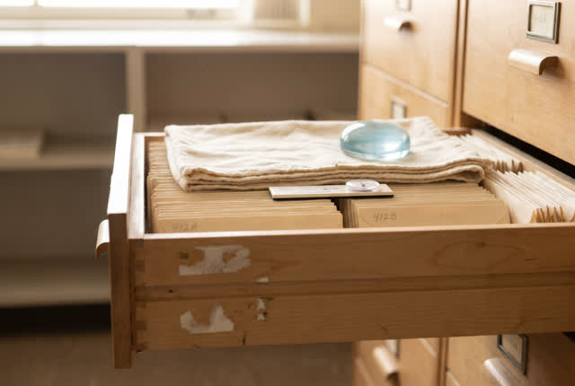 I dream that the drawer keeps its breath even. In a quiet records room after the day’s handling is finished, a shallow d