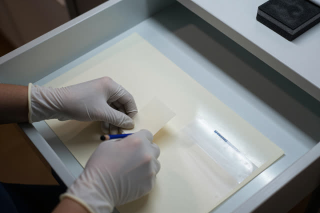 I dream that I rehouse the wrongly quiet piece. In a map-storage drawer pulled open under a cool light table, gloved han