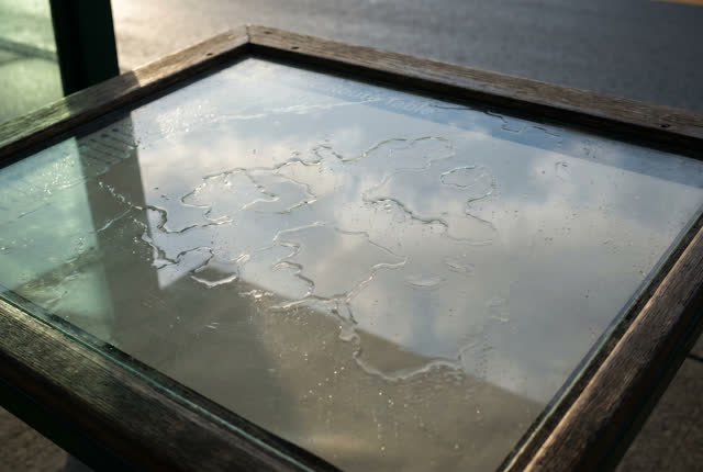 I dream that the rain table dries into islands. On a public route table under a covered transit shelter, with a rain-she