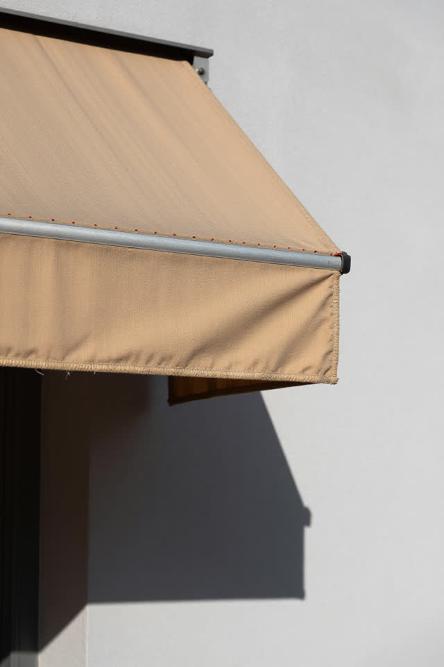 I dream that the awning patch waves only at the shadow. At a bright exterior shade edge over a public wall, with patched