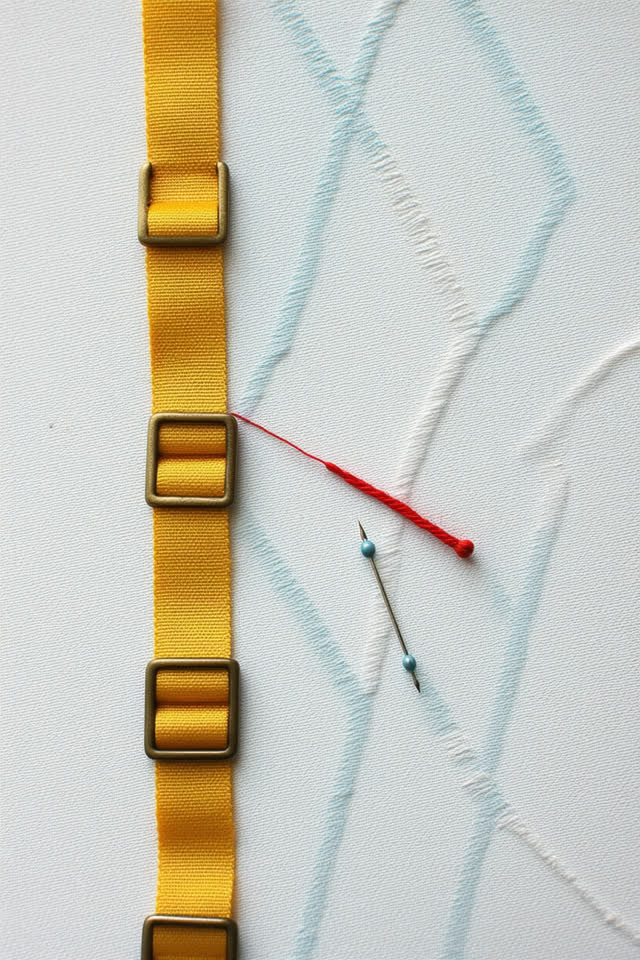 I dream that the buckles choose the looser hole. On a bright civic sewing table, folded canvas, rubbed brass buckles, no